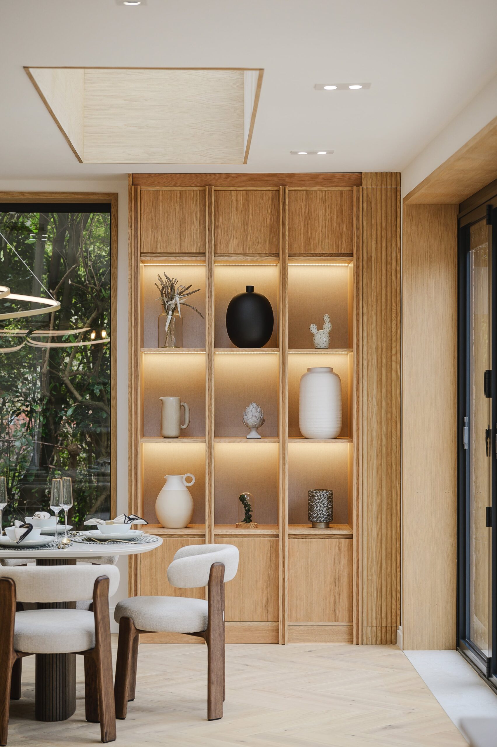 bespoke oak shelving with 9 shelves and contemporary accessories. Corner of white dining table with chairs