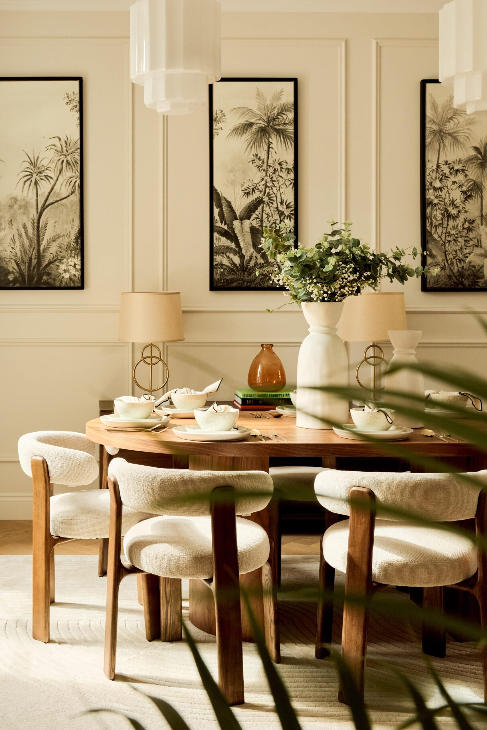 neutral interior dining room with large wooden table, beige boucle chairs, floral details and three artworks on wall