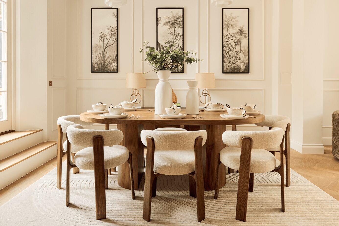 neutral interior dining room with large wooden table, beige boucle chairs, floral details and three artworks on wall