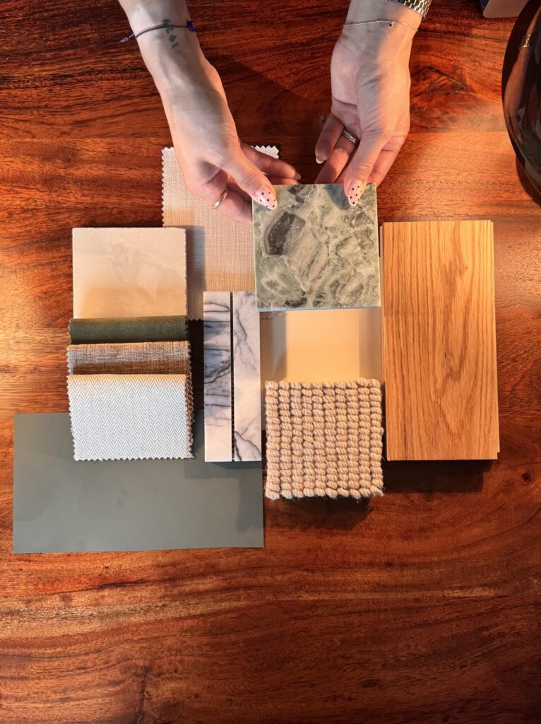 a selection of marble tile samples laid out on wooden table with two hands holding a tile birds eye camera view