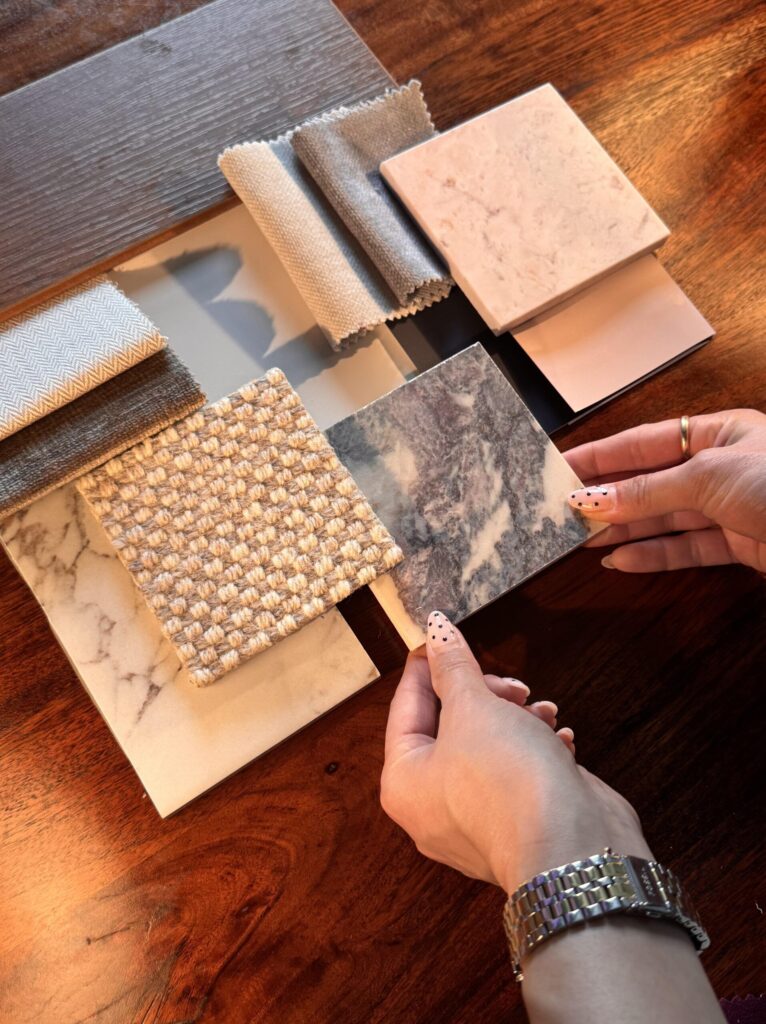 a selection of marble tile samples laid out on wooden table with two hands holding a tile birds eyes camera view