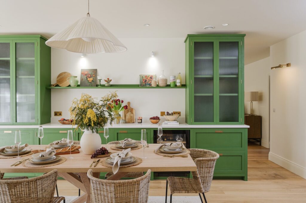 Modern kitchen interior with green cupboards, wooden dining furniture, pendant lighting and fresh flowers, styled for premium staging.